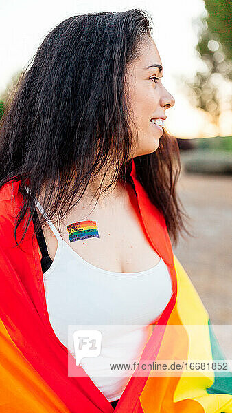 Glückliche Frau mit einer IGB-Flagge und einem Gay-Pride-Tattoo auf der Brust