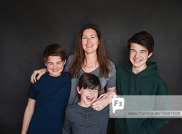 Mutter mit drei älteren Jungen  die vor einem schwarzen Hintergrund lachen.