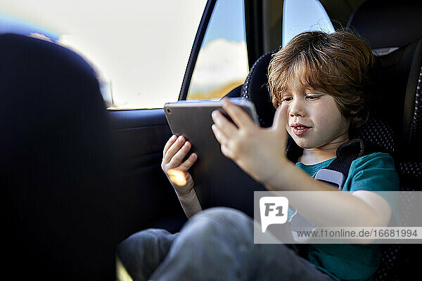 Niedlicher Junge  der ein digitales Tablet benutzt  während er am Wochenende im Auto unterwegs ist