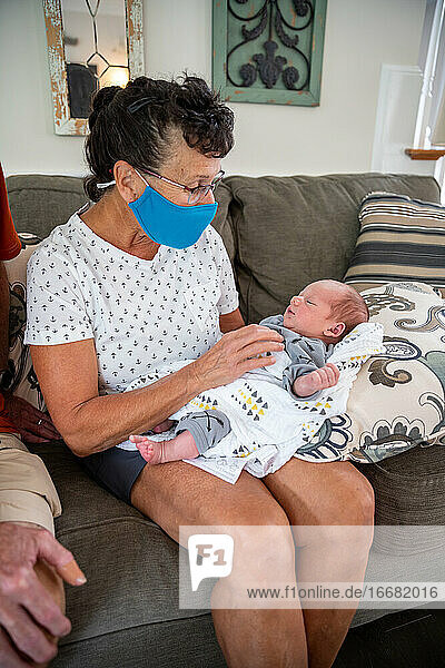 Woman wearing face mask holding newborn baby.