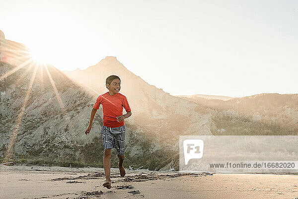 Latino tween boy running on beach with mountains in background