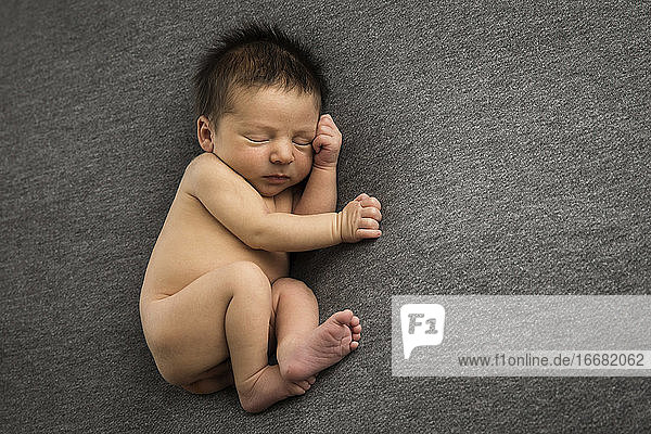 Neugeborener Junge mit vielen Haaren schläft auf grauem Hintergrund
