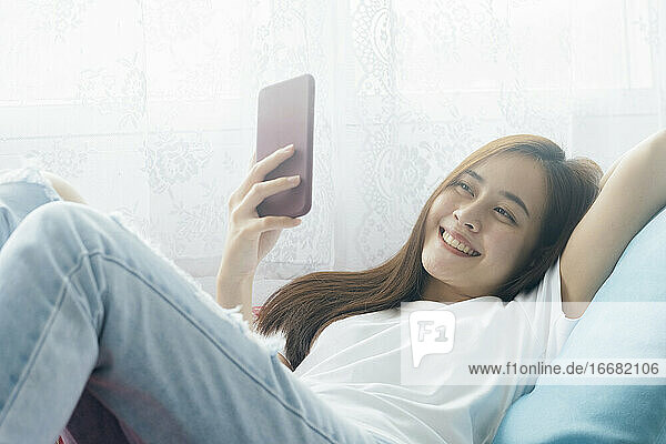 Attraktive lächelnde asiatische Frau mit Smartphone auf der entspannenden