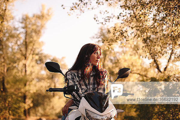 Porträt einer nachdenklichen  selbstbewussten jungen Frau auf einem Motorrad sitzend