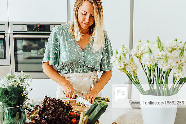 Junge kaukasische blonde Frau schneidet Gemüse am Küchentisch
