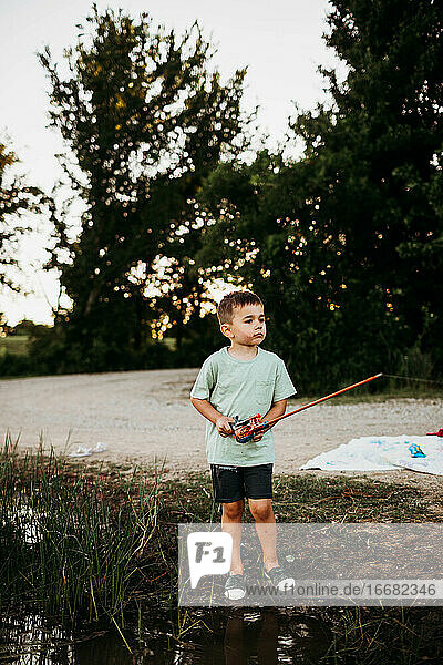 Junger Junge steht draußen am See und hält eine Angelrute