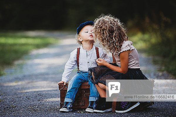 Adorable children siting on a vintage suitcase throwing a kiss