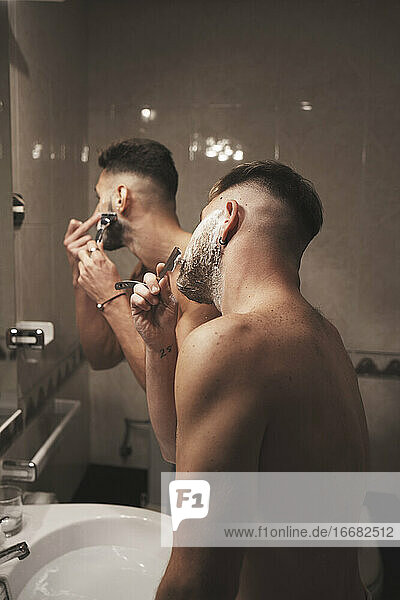 Side view of two men shaving together in the bathroom