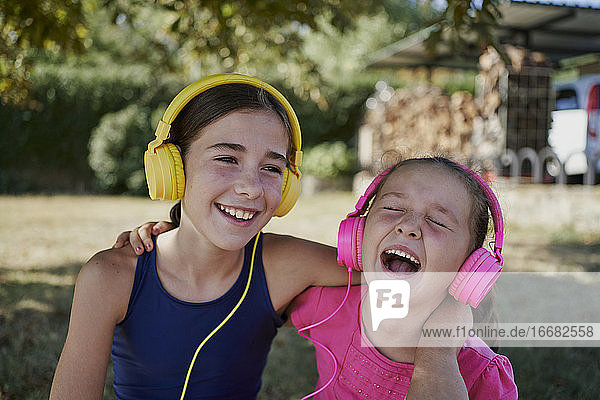 Kleine Mädchen hören Musik und lächeln mit gelben und rosa Kopfhörer in einem Garten. Glück Konzept