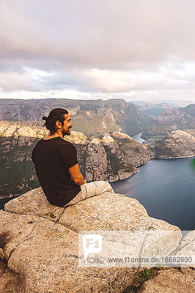 Man smiling sitting in rock at edge of cliff at Preikestolen  Norway
