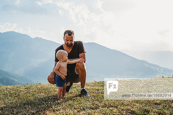 Weißer Vater kniend und Baby Junge in den Bergen mit Sonnenuntergang Licht