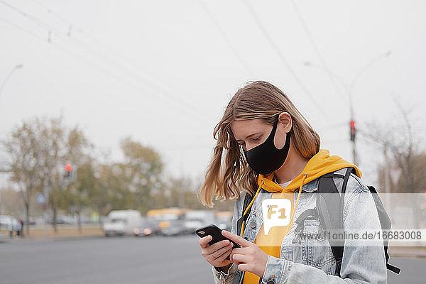 Porträt einer Frau mit Maske und Smartphone. Draußen im Freien sein