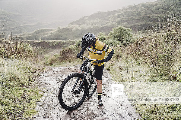 Ganzkörper-Radfahrerin auf schlammigem Bergpfad an einem regnerischen Tag