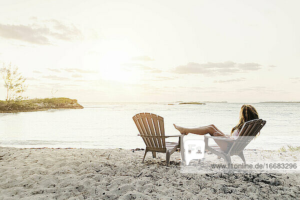Frau entspannt auf einem Stuhl am Strand gegen den Himmel bei Sonnenuntergang
