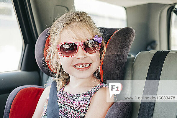Junges Mädchen mit Sonnenbrille in einem Autositz sitzend