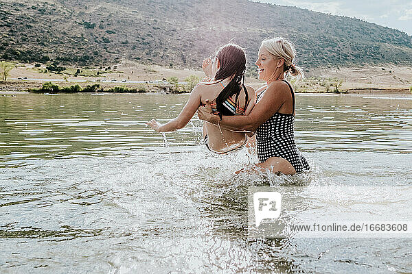 Mom tossing young daughter into lake on a sunny day