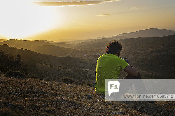Mann schaut bei Sonnenuntergang auf dem Gipfel eines Berges auf sein Smartphone