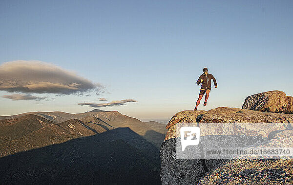 Mann läuft am Rande einer Klippe auf dem Gipfel eines Berges bei Sonnenuntergang in Maine