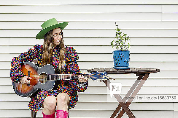 Eine schöne Frau sitzt an einem Tisch im Freien und spielt eine akustische Gitarre