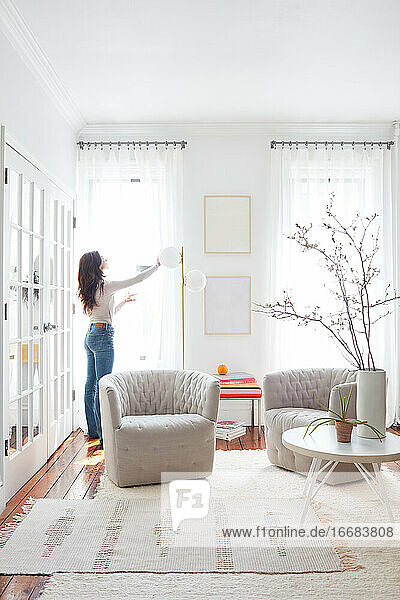 Frau verstellt Vorhänge in einem weißen  hellen Raum mit modernen Möbeln