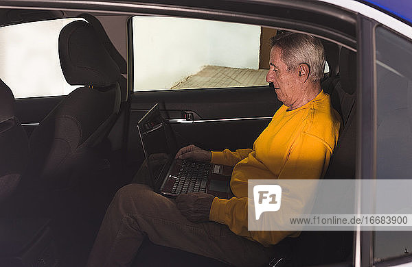 Ein älterer Mann benutzt einen Laptop auf dem Rücksitz des Autos