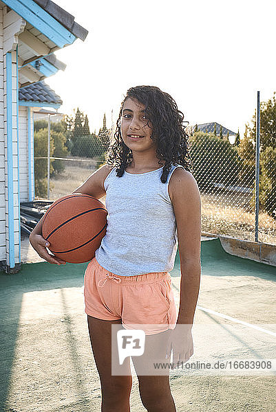 Ein kleines Mädchen mit einem Basketball mit dem Sonnenuntergang im Hintergrund