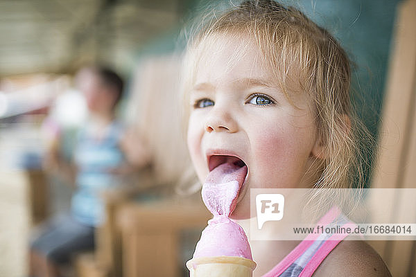 Junges süßes Mädchen leckt fröhlich rosa Eis am Sommertag.