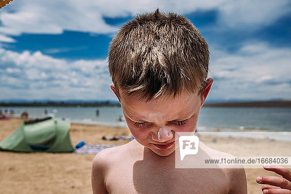 Nahaufnahme eines Jungen am Strand mit Sonnenschutzmittel auf der Nase