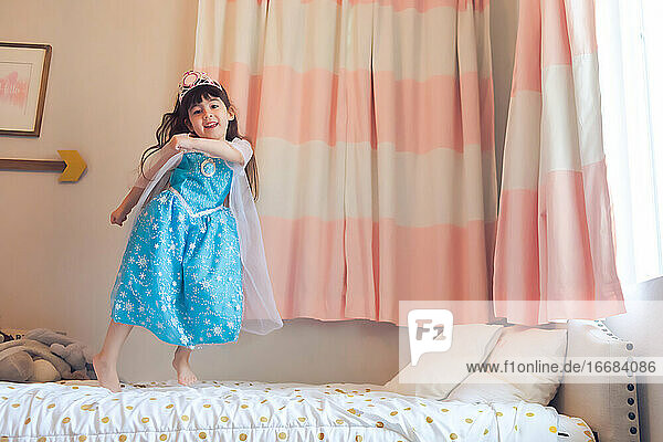 Kleines Mädchen als Prinzessin verkleidet tanzt und springt auf ihrem Bett.
