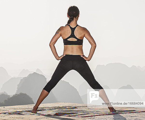 schöne Frau  die oberhalb der kastigen Berge von Yangshuo Yoga praktiziert