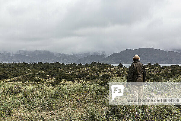 An older man looks out across a shallow bay.
