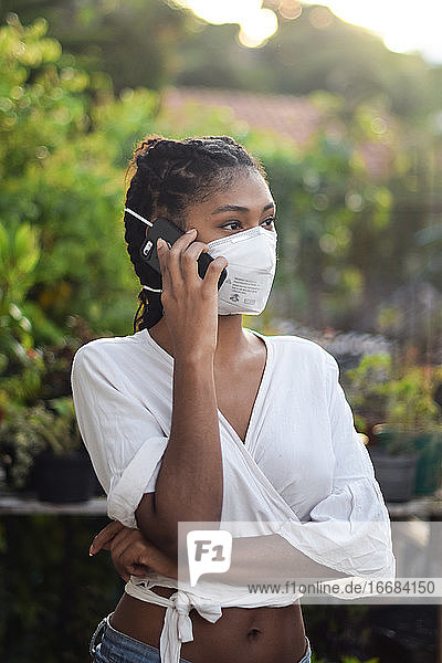 Junge schwarze Frau mit Gesichtsmaske spricht am Telefon