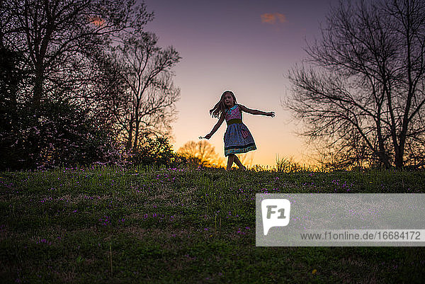 Kleines Mädchen tanzen Sonnenuntergang Gras Blumen Silohette Hügel Bäume wirbelnden