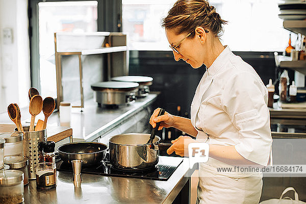 Weibliche Köchin bei der Arbeit in der Restaurantküche  rührt heißes Essen in der Pfanne um