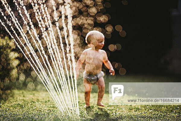 Bokeh Baby im Garten spielen mit Wasser aus Sprinkler