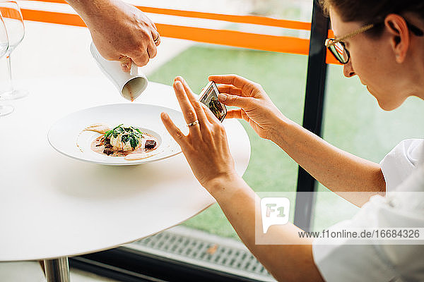 Frau fotografiert Essen mit Smartphone  während der Kellner das Essen serviert