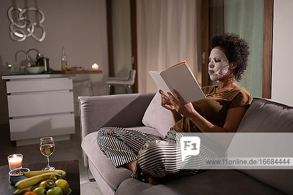 Afroamerikanische Frau mit Bettlakenmaske liest ein Buch