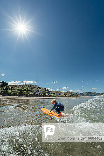 Kleines Kind beim Surfen in Neuseeland an einem sonnigen Tag
