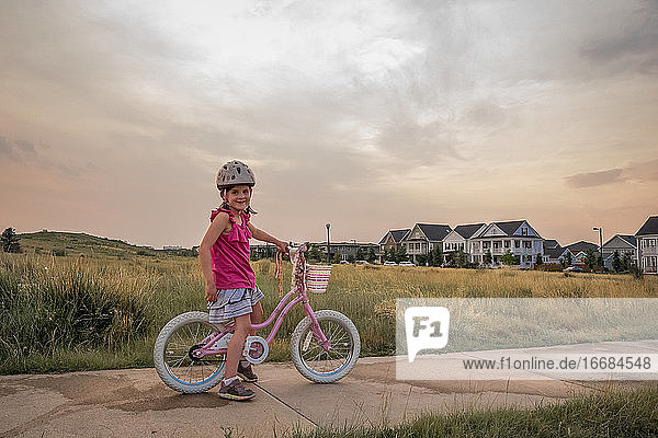 portrait of smiling young girl sitting on her bike in a park at sunset