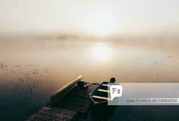 Leerer Steg mit festgemachten Booten an einem nebligen Morgen auf einem ruhigen See.