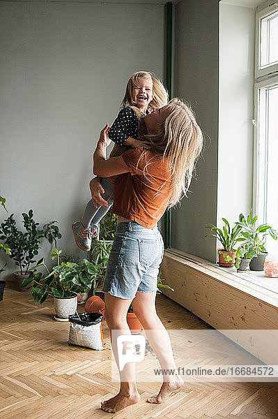 Woman holds in hugs her laughing child in living room with lot plants