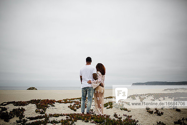 Mixed Race Couple Embracing on Sand Dunes Maternity