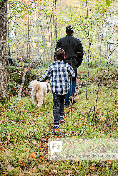 Boy and his father and dog hiking through the woods on a fall day.