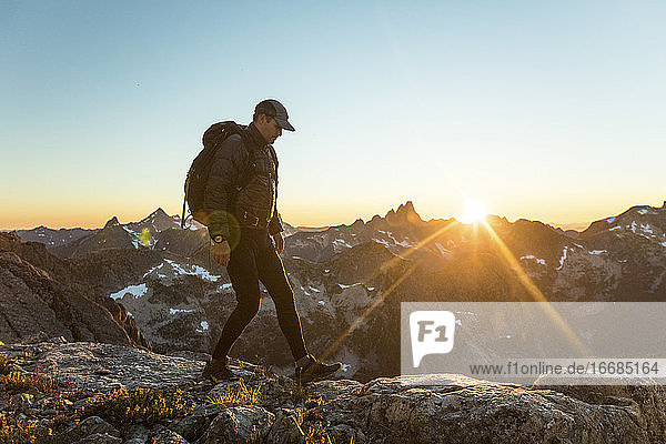Adventurous man hiking along mountain ridge during sunset.