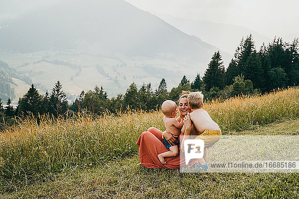 Children hugging their mother with mountains in the back in summer