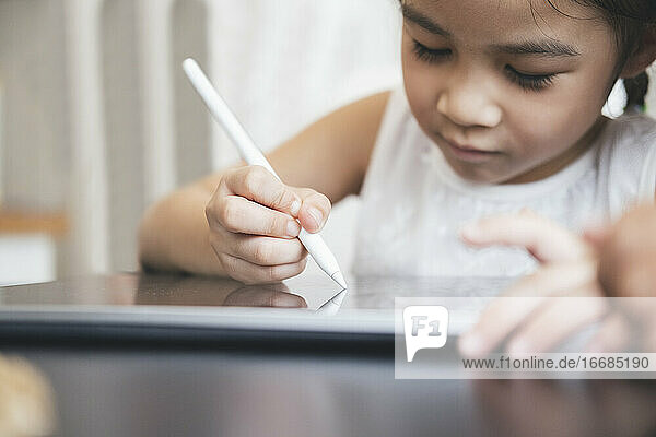 Kleines Mädchen mit Tablet und Stift lernt online zeichnen
