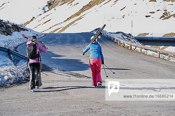 two skiers carry their skis on their shoulders along the road