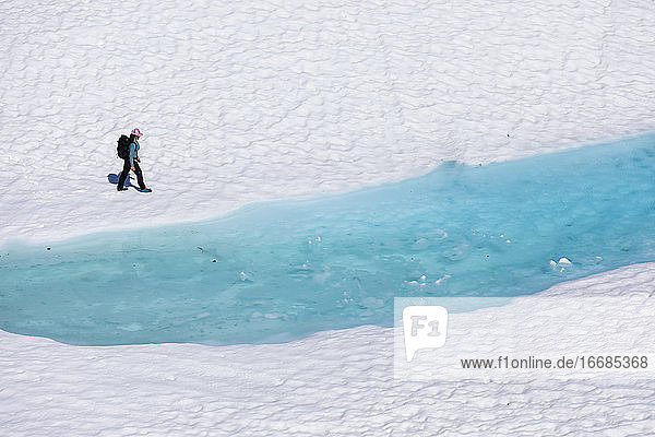 Drohnenansicht einer nicht erkennbaren Wanderin  die während ihres Urlaubs in British Columbia an einem schmelzenden See mit klarem  blauem Wasser entlang läuft