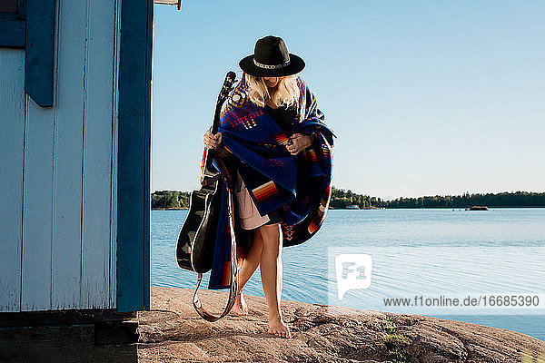Frau in eine Decke gewickelt  die ihre Gitarre am Strand hält