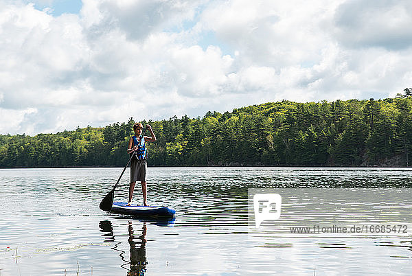 Teen boy paddling on a SUP on lake in Ontario  Canada on a sunny day.